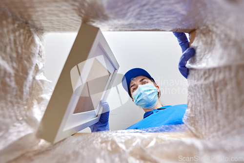 Image of woman in mask packing photo frame to parcel box