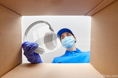 Image of woman in mask packing headphones into parcel box