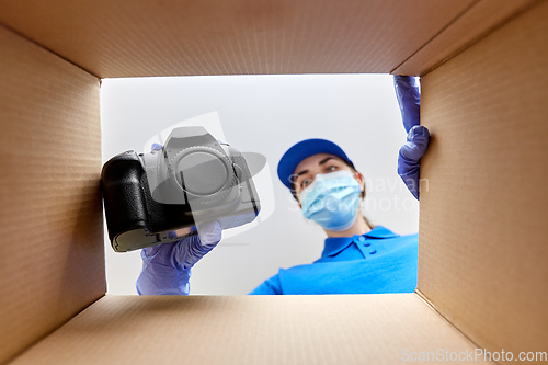 Image of woman in mask packing camera into parcel box