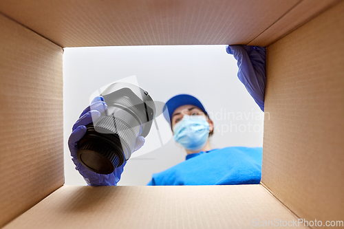 Image of woman in mask packing camera into parcel box