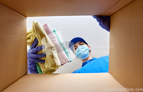 Image of woman in mask packing clothes to parcel box