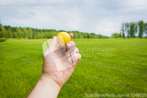 Image of Hand with golf ball over a golf course