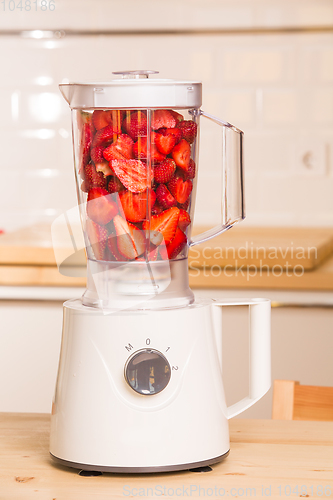 Image of fresh strawberries in white Blender on a wooden table