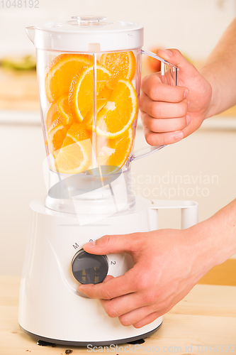Image of White blender with juicy oranges on a wooden table