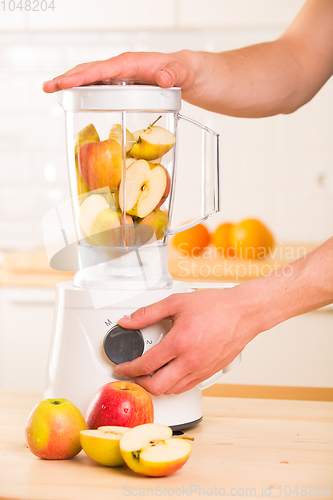 Image of White blender with apples on a wooden table.