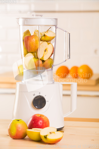 Image of White blender with apples on a wooden table.