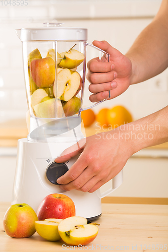 Image of White blender with apples on a wooden table.