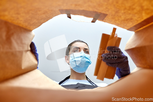 Image of saleswoman in gloves and mask packing food in bag