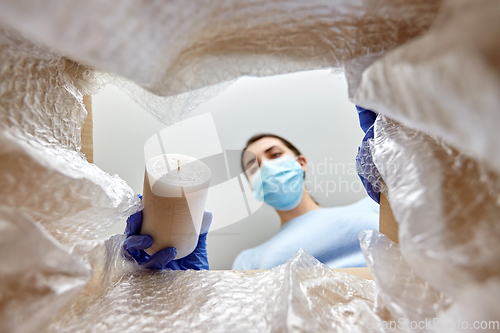 Image of woman in mask packing candles into parcel box