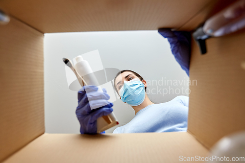 Image of woman in mask unpacking parcel box with cosmetics