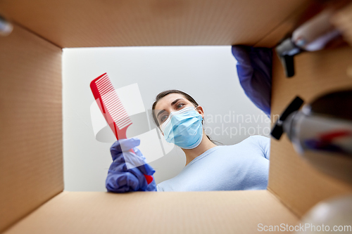 Image of woman in mask unpacking parcel box with cosmetics