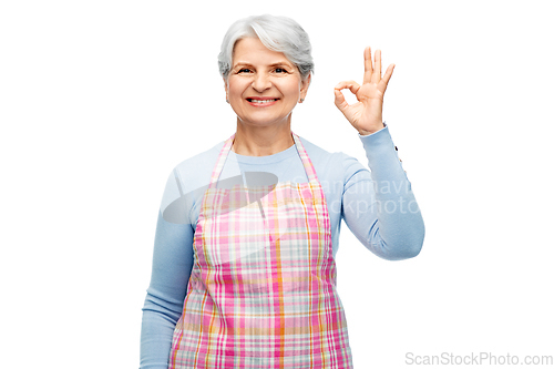 Image of smiling senior woman in apron showing ok gesture