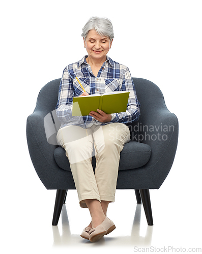 Image of smiling senior woman in armchair writing to diary