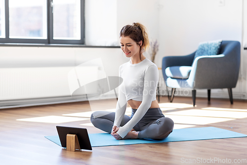 Image of young woman with tablet pc doing yoga at home