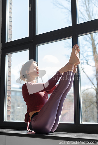 Image of woman doing yoga exercise on window sill at studio