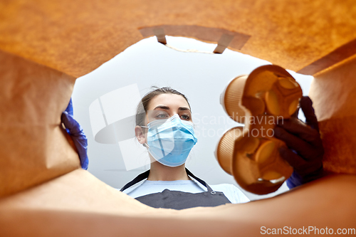 Image of saleswoman in gloves and mask packing food in bag