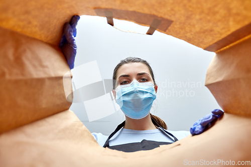 Image of saleswoman in gloves and mask packing food in bag