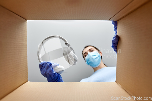 Image of woman in mask packing headphones into parcel box