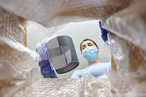 Image of woman in mask opening parcel box with flower pot