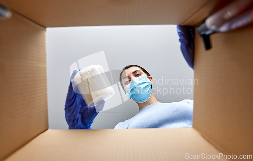 Image of woman in mask unpacking parcel box with cosmetics