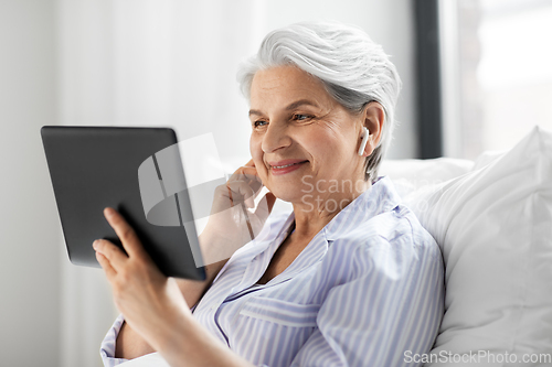Image of senior woman with tablet pc and earphones in bed