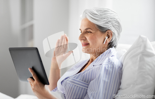 Image of old woman with tablet pc having video call in bed