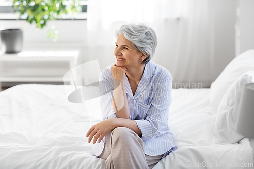 Image of happy senior woman sitting on bed at home bedroom