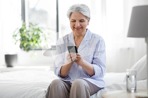 Image of happy senior woman with smartphone on bed at home