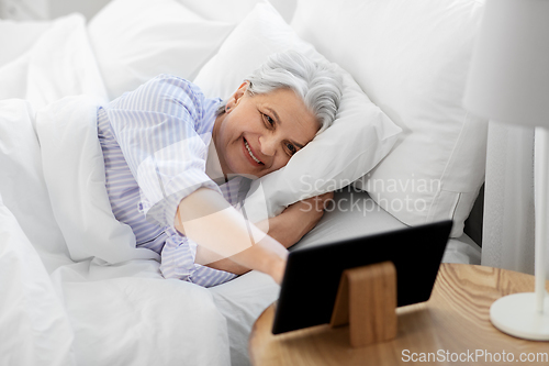 Image of happy senior woman with tablet pc in bed at home