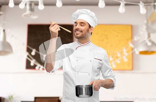Image of happy smiling male chef with saucepan tasting food