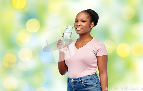 Image of happy african woman drinks water from glass bottle