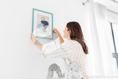 Image of woman on ladder decorating home with art