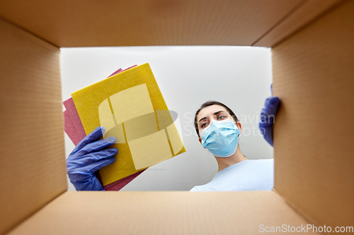 Image of woman in mask taking cleaning supplies from box