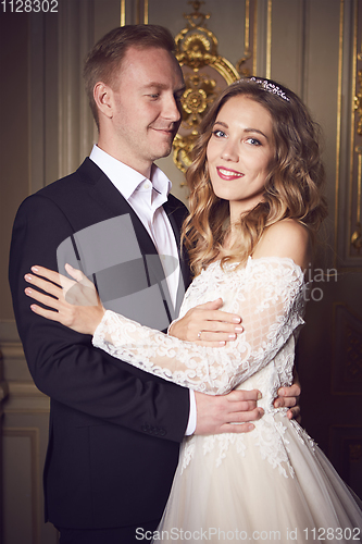 Image of Wedding couple indoors is hugging each other. Beautiful model girl in white dress. Man in suit. Beauty bride with groom. Female and male portrait. Woman with lace veil. Cute lady and handsome guy