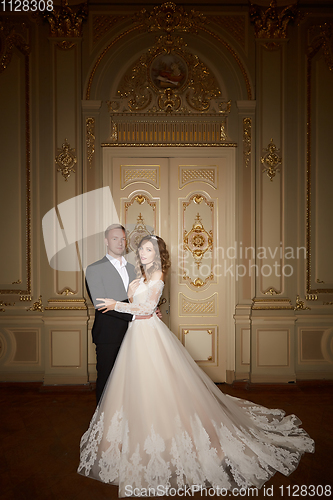 Image of Charming wedding couple in interior in Baroque style is hugging each other on great royal palace