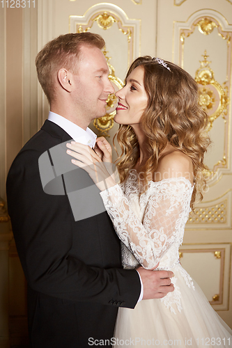 Image of Wedding couple indoors is hugging each other. Beautiful model girl in white dress. Man in suit. Beauty bride with groom. Female and male portrait. Woman with lace veil. Cute lady and handsome guy