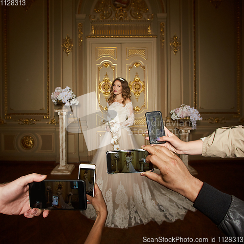 Image of Guests take photographs of the bride on smartphones. Focus on smartphones.