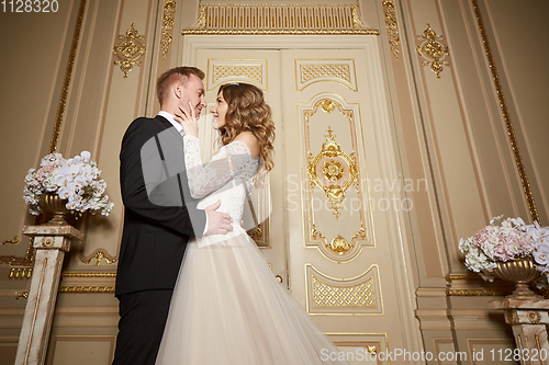 Image of Wedding couple indoors is hugging each other. Beautiful model girl in white dress. Man in suit. Beauty bride with groom. Female and male portrait. Woman with lace veil. Cute lady and handsome guy