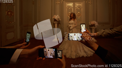 Image of Guests take photographs of the bride on smartphones. Focus on smartphones.