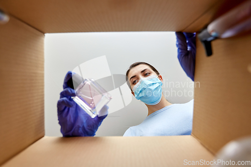 Image of woman in mask unpacking parcel box with cosmetics