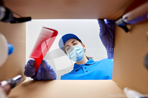 Image of woman in mask packing parcel box with cosmetics