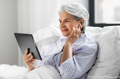 Image of senior woman with tablet pc and earphones in bed