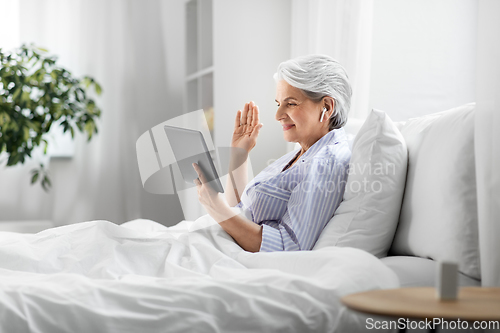 Image of old woman with tablet pc having video call in bed