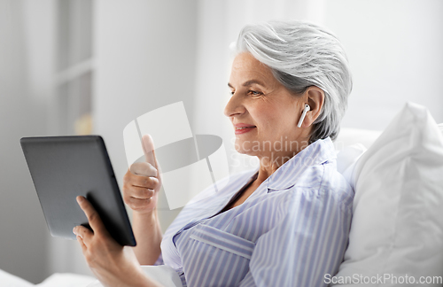 Image of old woman with tablet pc having video call in bed