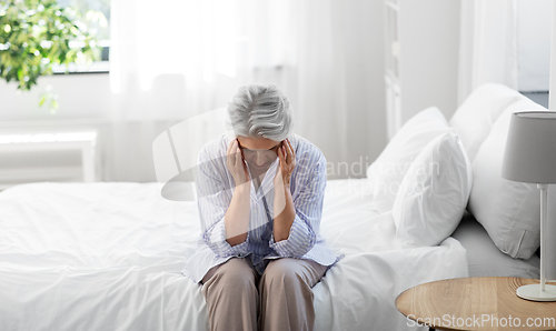 Image of senior woman with headache sitting on bed at home