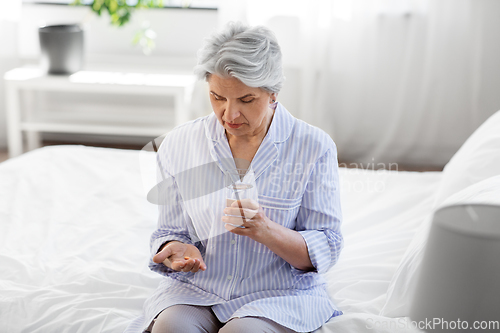 Image of senior woman with pill and water sitting on bed