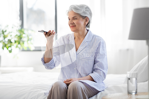 Image of happy senior woman recording voice on smartphone