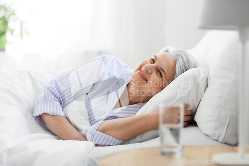 Image of happy senior woman lying in bed at home bedroom