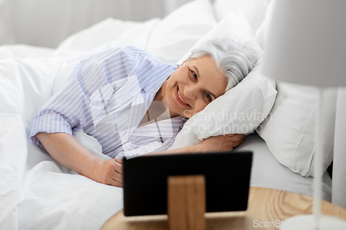 Image of happy senior woman with tablet pc in bed at home