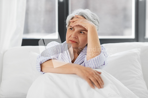 Image of senior woman with headache sitting in bed at home